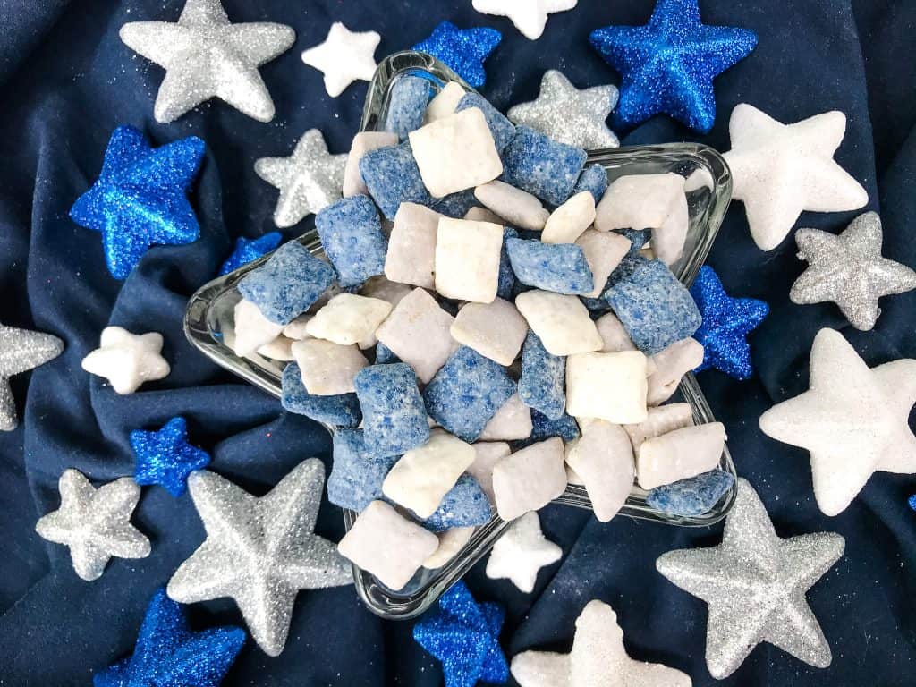 Blue, gray, and white muddy buddies in a dish surrounded by colored glitter stars