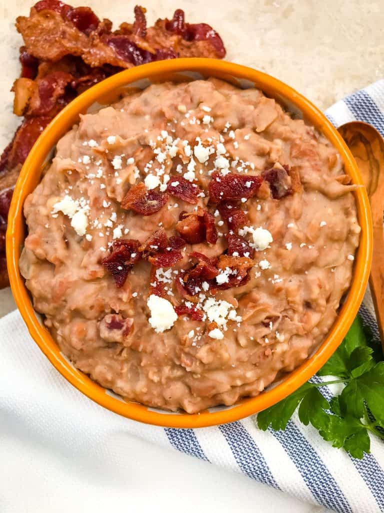 A yellow bowl filled with Homemade Bacon Refried Beans on a towel