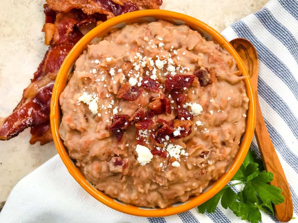 Refried beans in a bowl on a towel with bacon next to it
