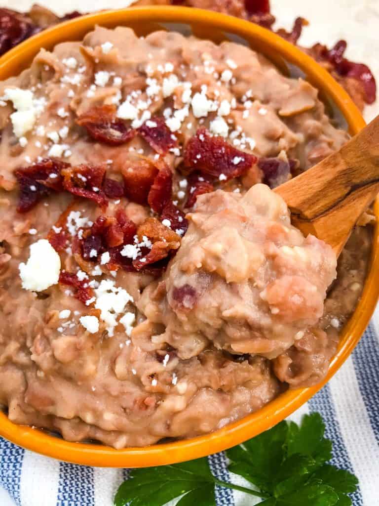Close up of Homemade Bacon Refried Beans with a spoon scooping some beans out