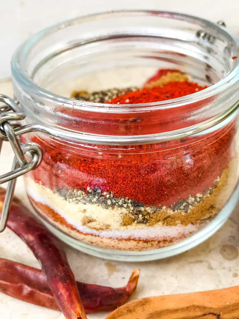 A close up of a clear jar with layered spices to make Homemade Taco Seasoning