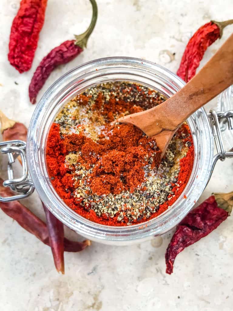 A jar from top view with layered spices for Homemade Taco Seasoning with wooden spoon