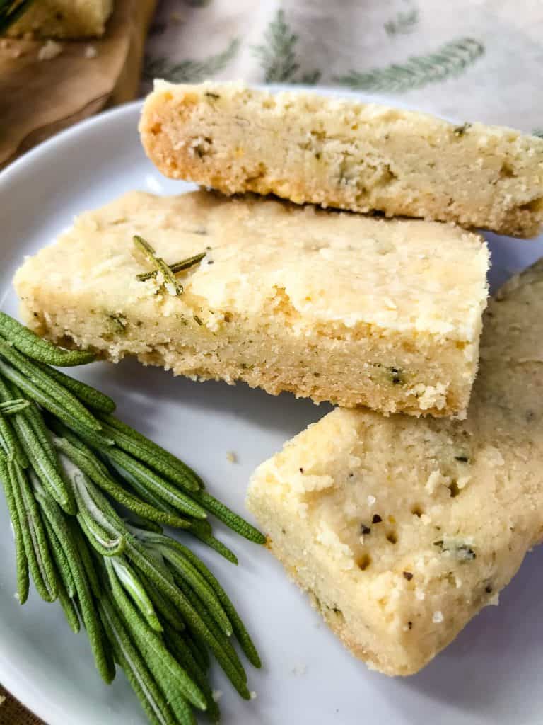 Close up of three Olive Oil Rosemary Shortbread on a plate with rosemary branch