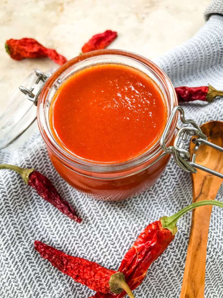Jar of Red Enchilada Sauce Recipe surrounded by red peppers