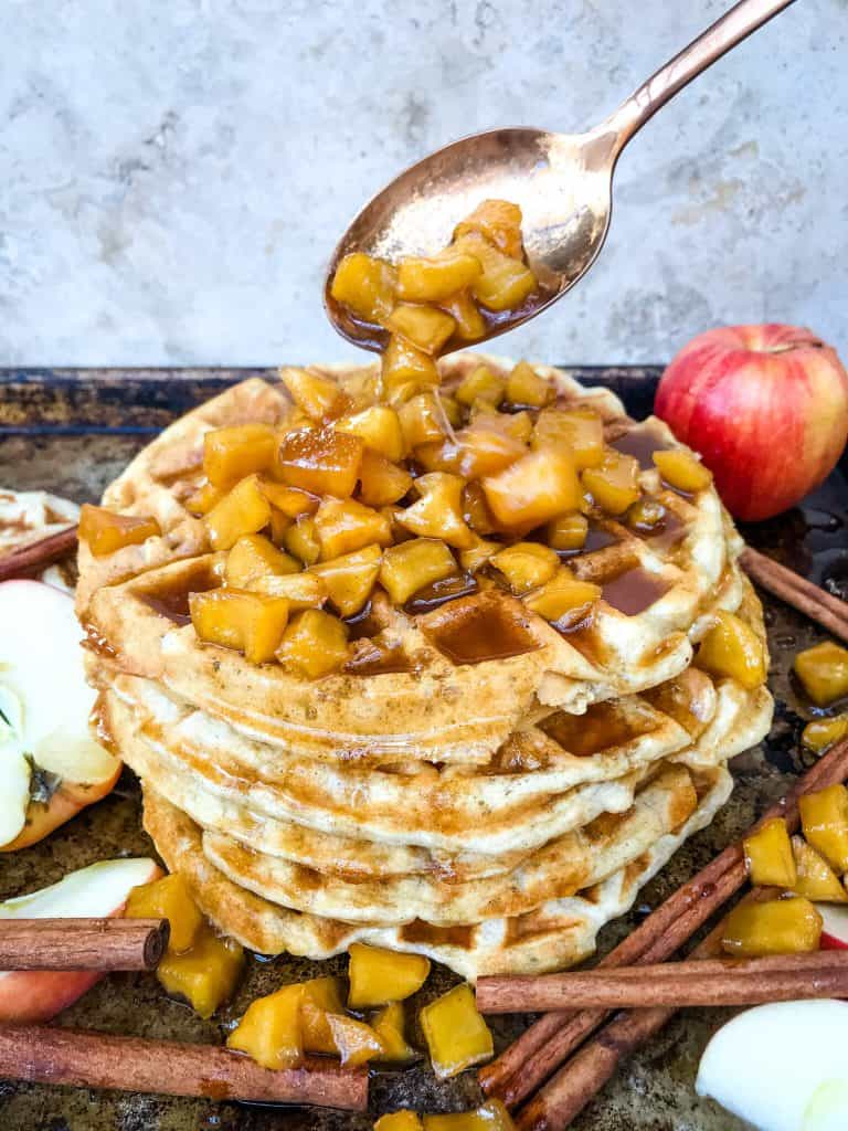 A spoon pouring cinnamon apple sauce over a waffle stack