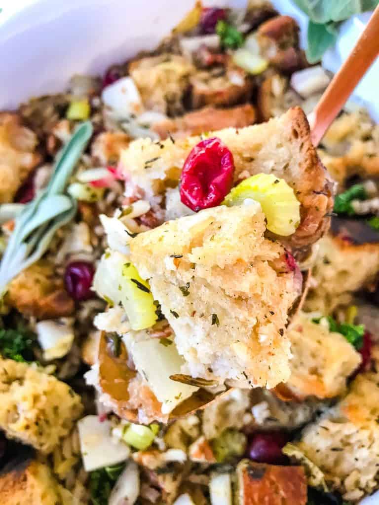 A spoon scooping Thanksgiving Stuffing with Cranberries, Kale, Pecans, and Wild Rice out of the dish