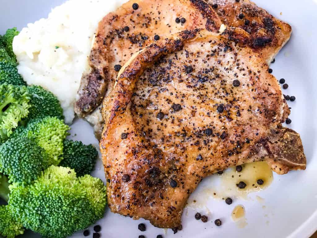 A close up of two pork chops with broccoli and potatoes