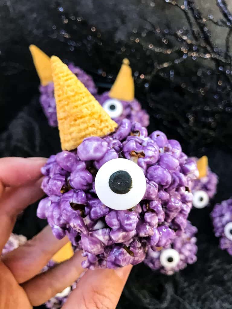 A hand holding a Purple People Eater Halloween Popcorn Ball
