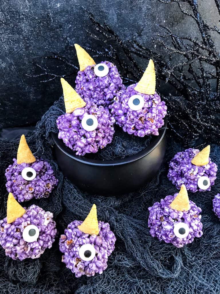 Purple People Eater Halloween Popcorn Balls in a cauldron and around it on gray gauze fabric