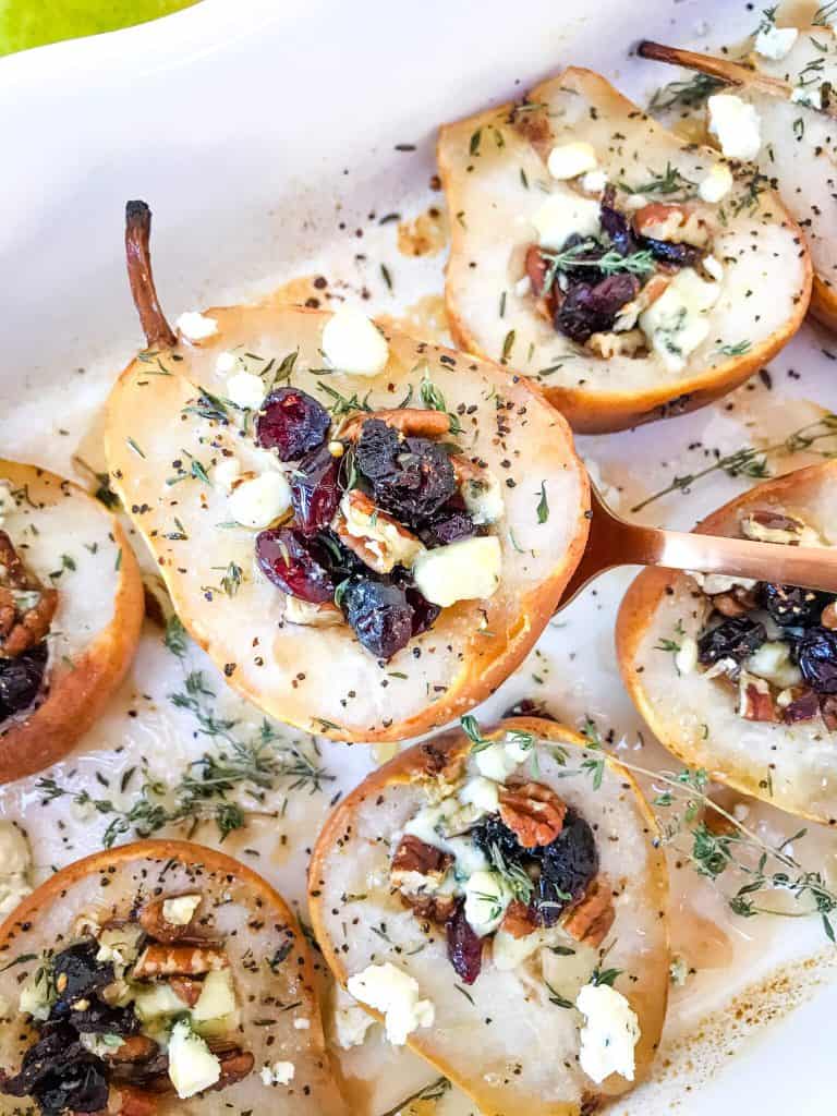 A spoon scooping a savory baked pear out of a baking dish