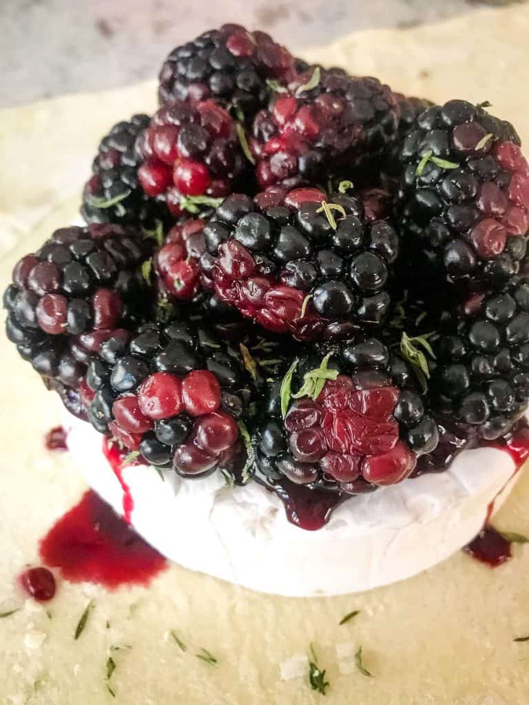 A brie wheel sitting on puff pastry, topped with jam and blackberries