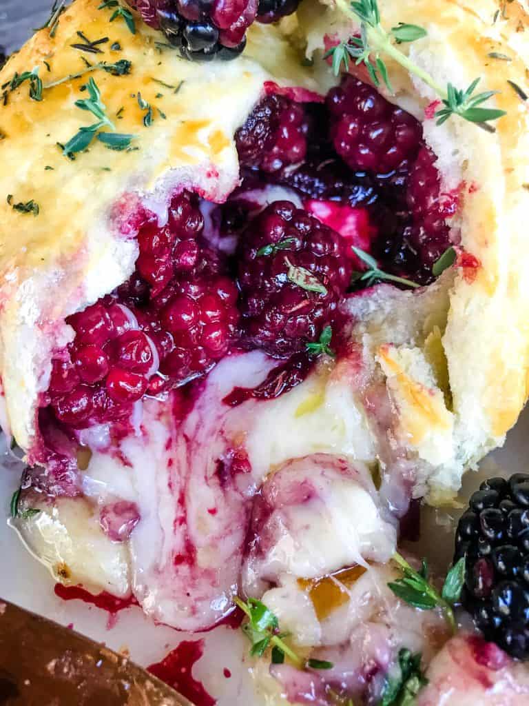 A close up of Thyme Blackberry Baked Brie in Puff Pastry cut open with berries and cheese oozing out