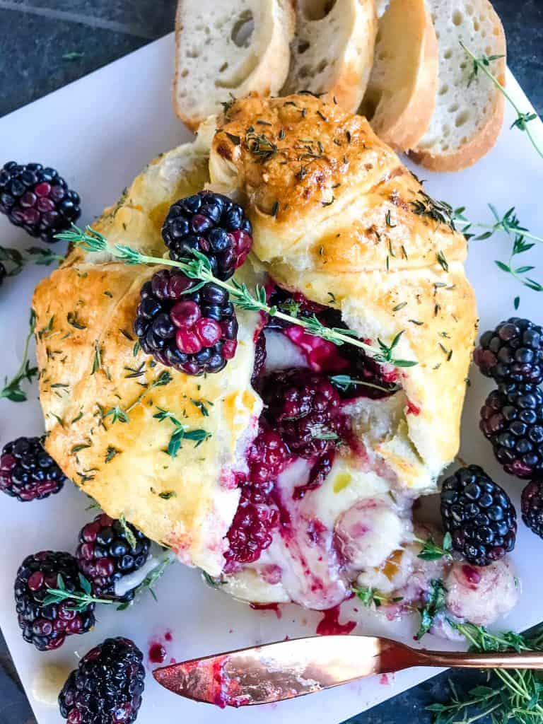 A Thyme Blackberry Baked Brie in Puff Pastry cut open with cheese oozing out on a marble board