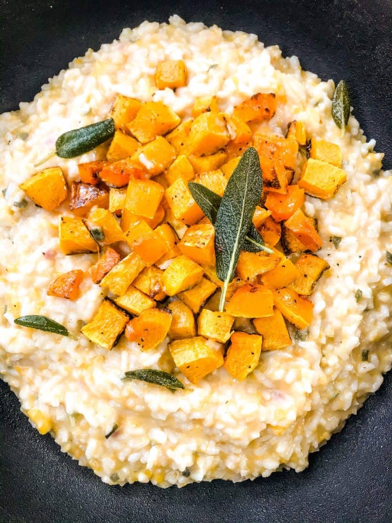 A black bowl filled with Butternut Squash Sage Risotto and topped with sage leaves and squash cubes.