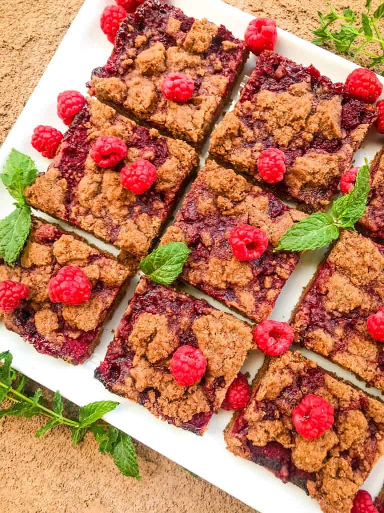 Squares of Chocolate Raspberry Crumble Bars on a white tray with fresh raspberries and mint around them