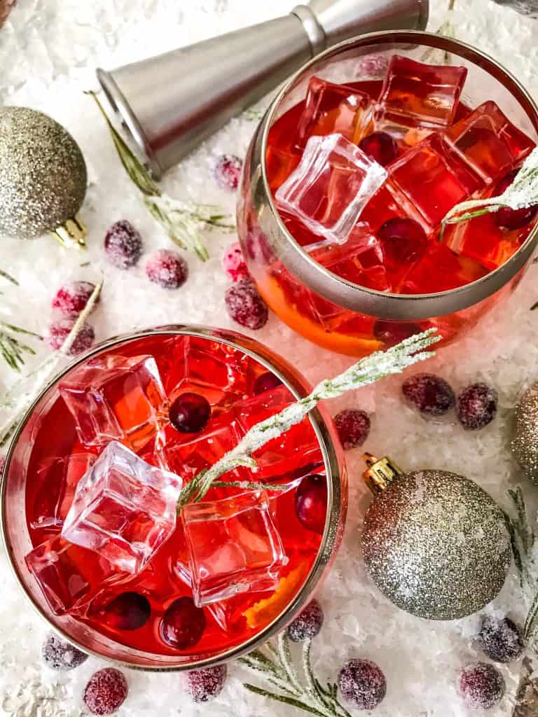 Top view of two glasses of Cranberry Old Fashioned Cocktail surrounded by cranberries on white snow