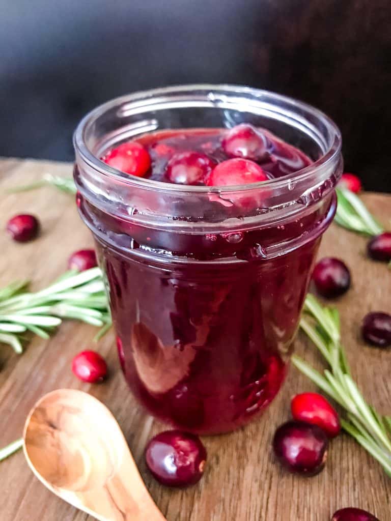 A jar of Cranberry Simple Syrup surrounded by cranberries