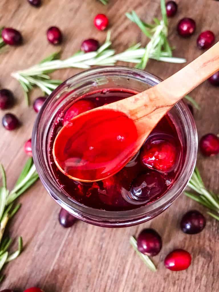 A wood spoon scooping Cranberry Simple Syrup in a jar