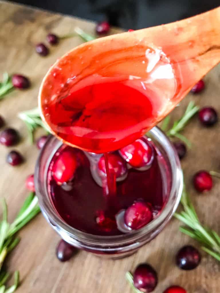 A spoon pouring red syrup into a jar