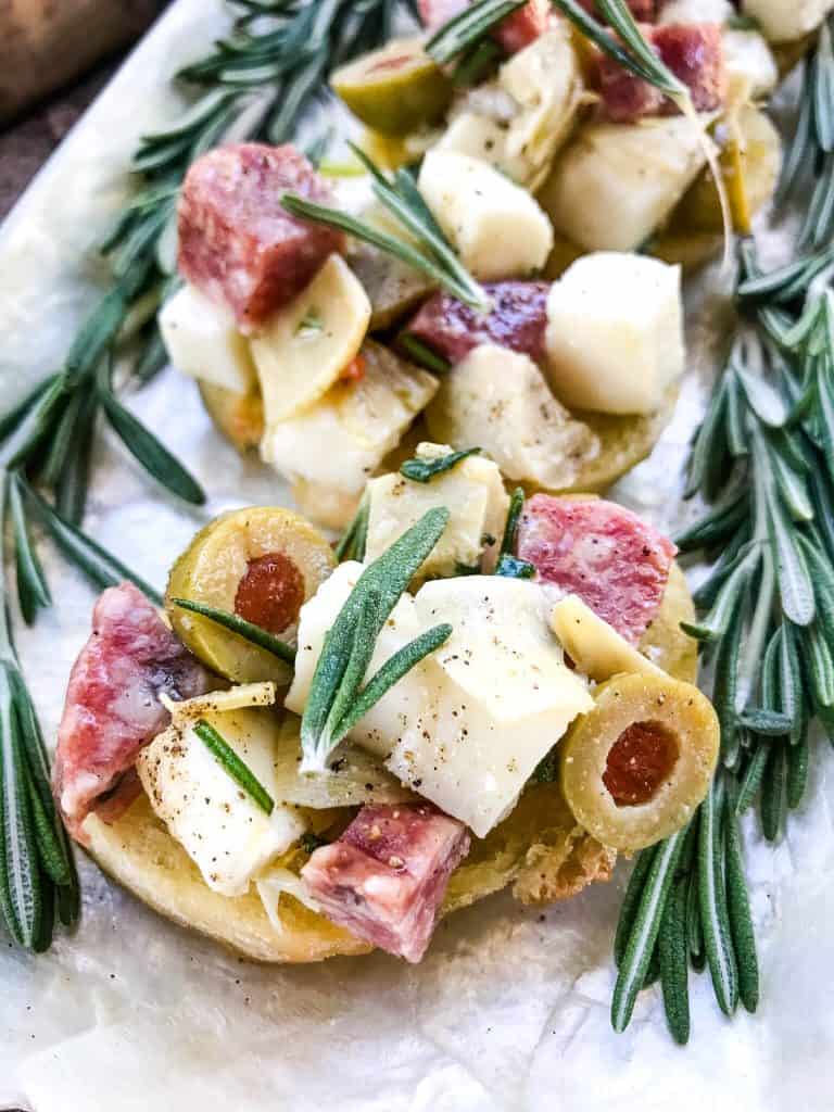 Antipasti Crostini lined up on a plate with rosemary around them