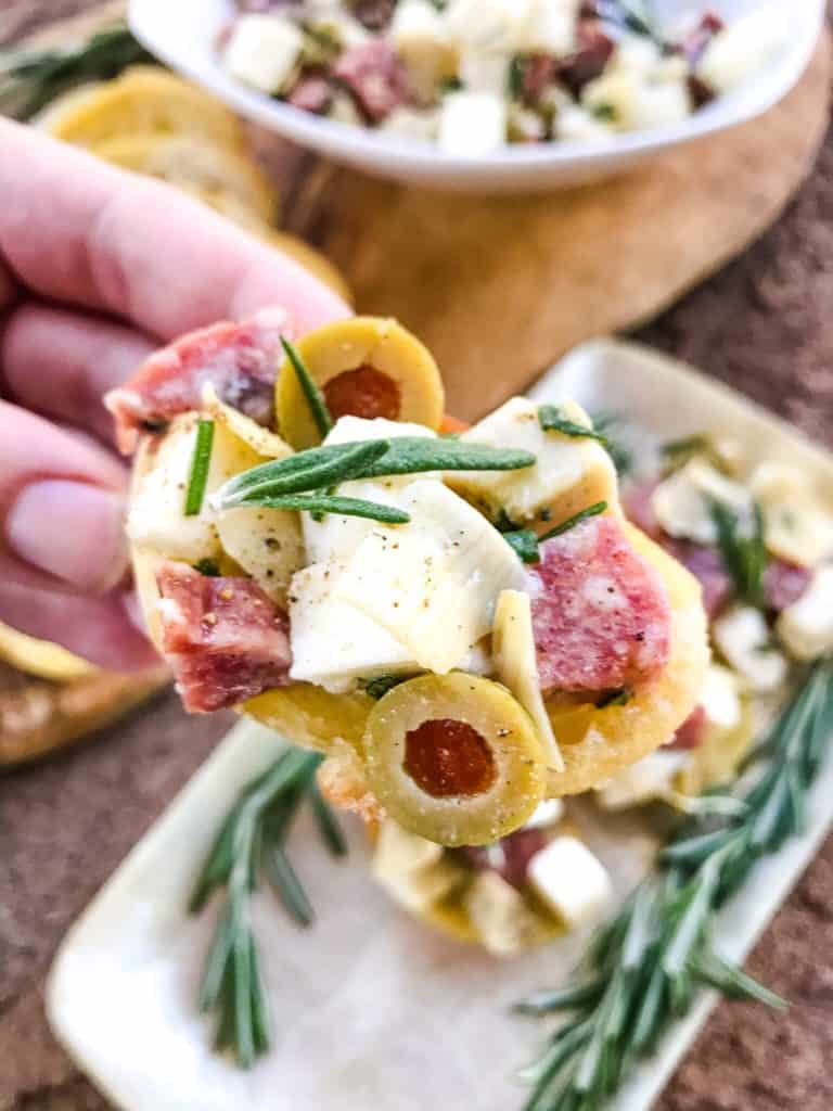 A hand holding a piece of Antipasti Crostini