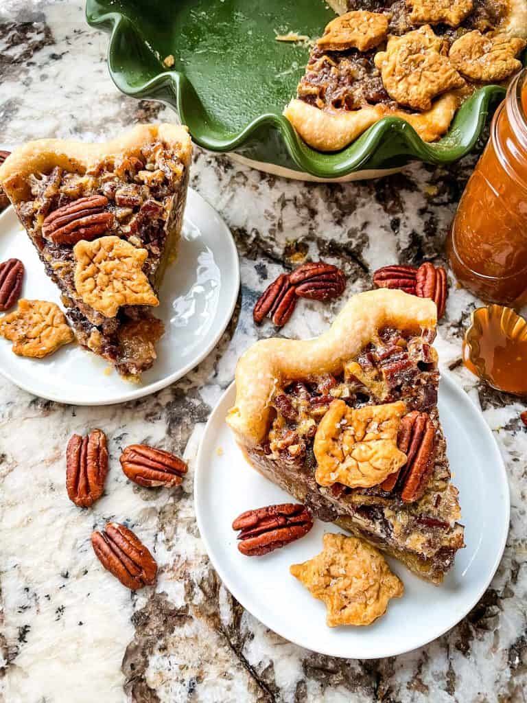 Two slices of pecan pie on small plates with the pie dish in the corner