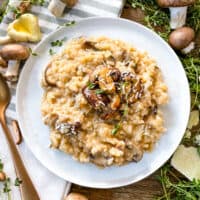 Creamy Mushroom Risotto on a white plate surrounded by mushrooms and fresh thyme