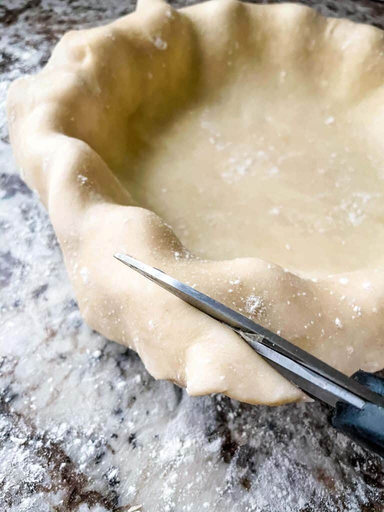 Scissors cutting the excess crust off a pie crust