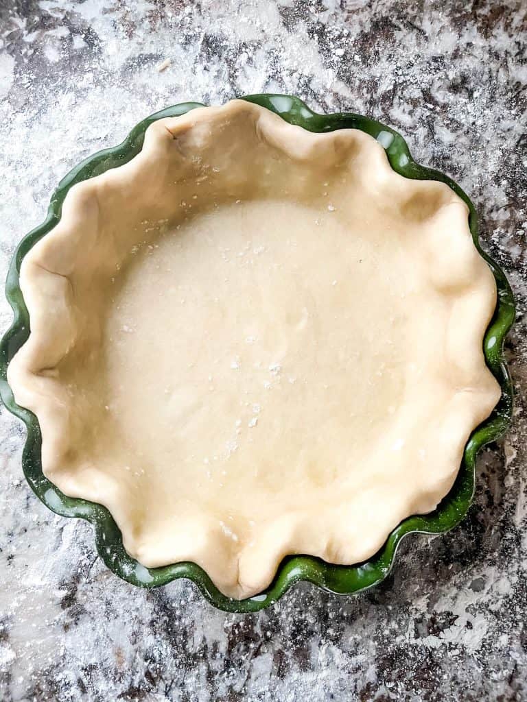 A pie crust dough in a green fluted pie dish