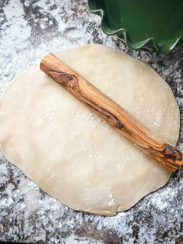 A rolling pin on top of a round piece of pie dough on a granite counter