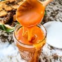 A copper spoon pouring Salted Whiskey Caramel Sauce in a small jar
