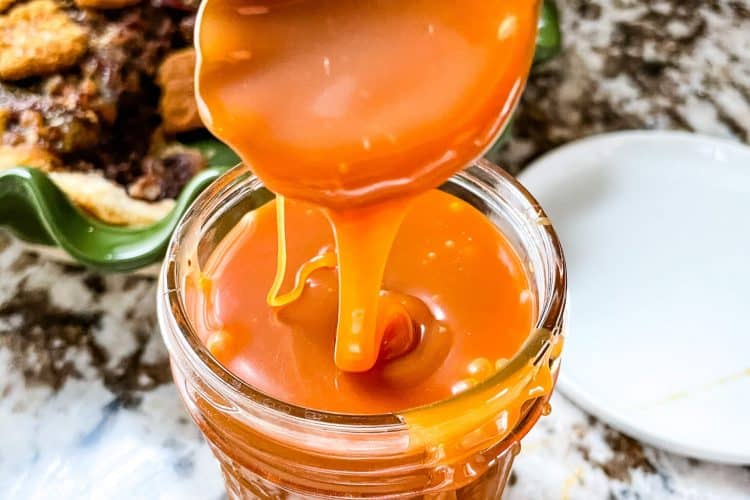 A copper spoon pouring Salted Whiskey Caramel Sauce in a small jar
