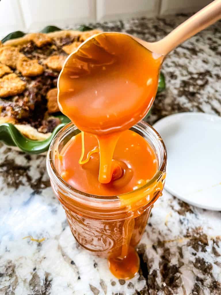 A copper spoon pouring Salted Caramel Whiskey Sauce into a small glass jar