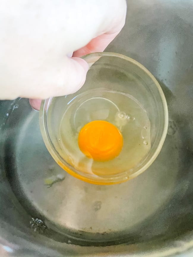 Cooking Poached Eggs by dropping an egg in a small bowl into hot water