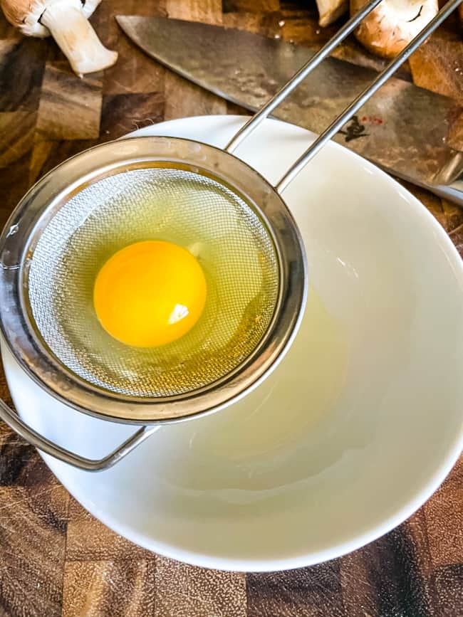 Cooking Poached Eggs by an egg straining over a bowl