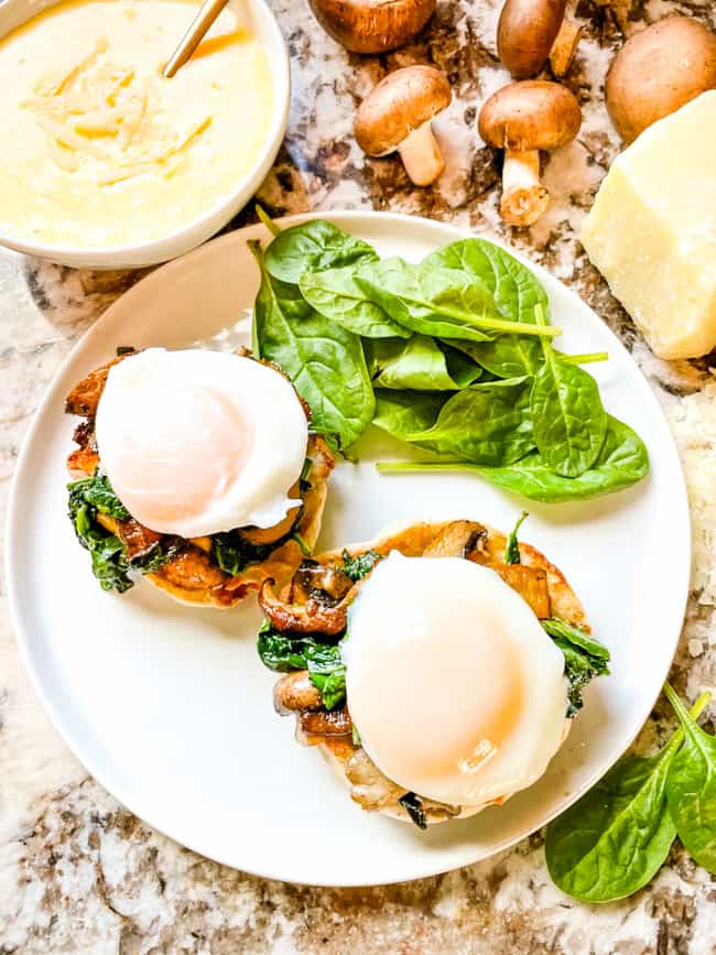 Two stacks of the benedict from the top on a white plate without sauce, and some spinach on the side