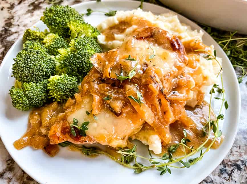 A French Onion Pork Chop on a plate with potatoes and broccoli