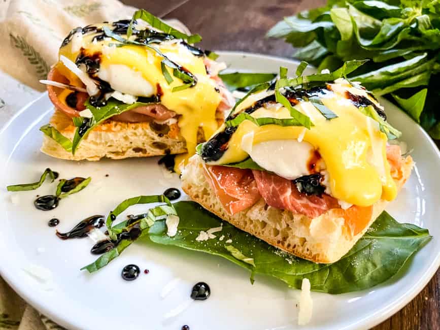 Side view of two benedict stacks on a white plate with basil and balsamic