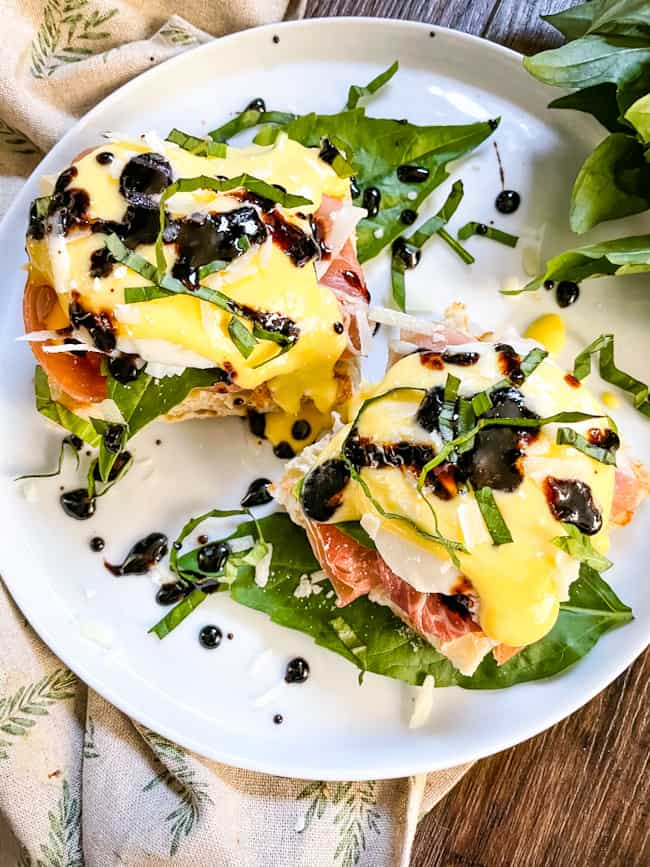 Top view of two stacks of Italian Prosciutto Eggs Benedict on a white plate with basil around it