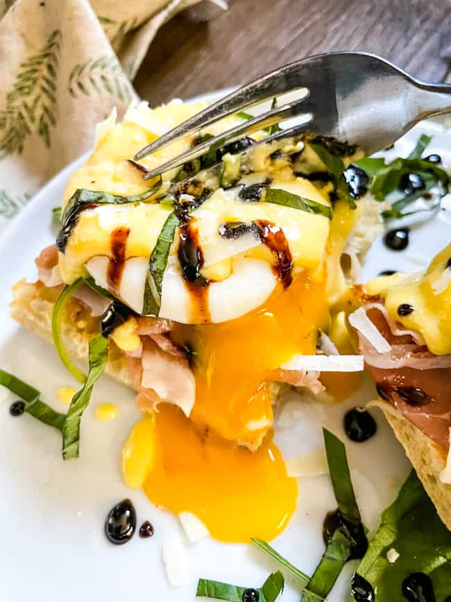 A fork cutting into an egg with the yolk running over the food and plate