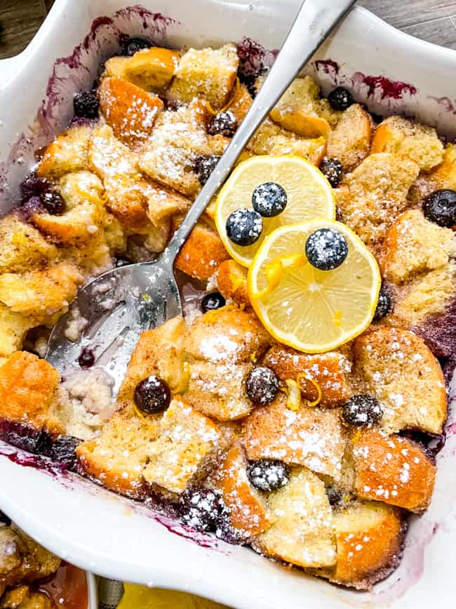 A white dish full of Lemon Blueberry Bread Pudding with a spoon in it