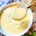 A spoon scooping Blender Parmesan Cheese Hollandaise Sauce out of a bowl