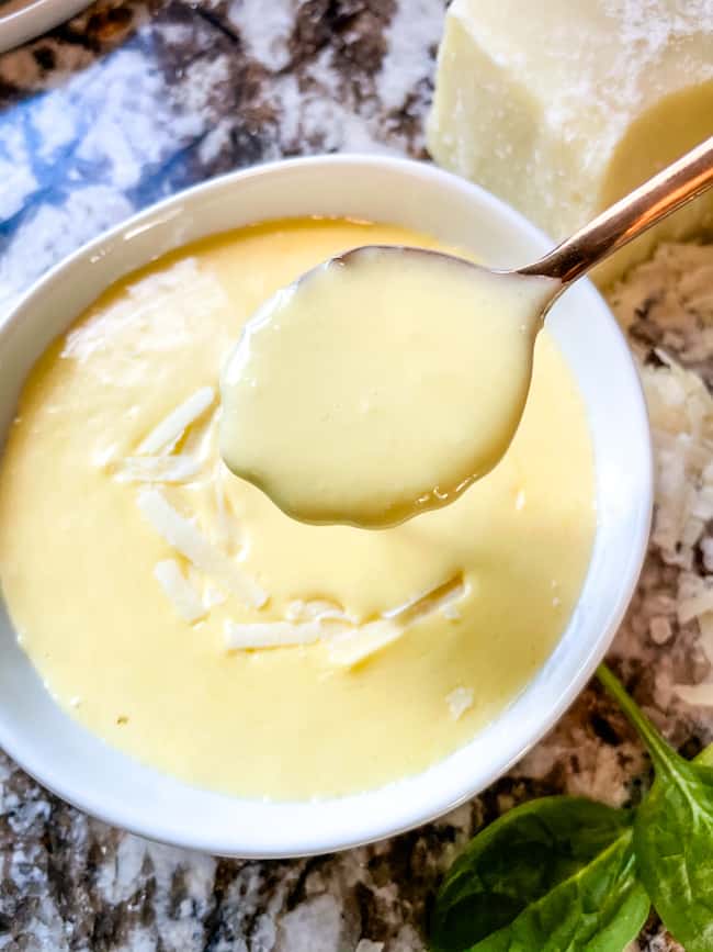 A spoon scooping Blender Parmesan Cheese Hollandaise Sauce out of a bowl