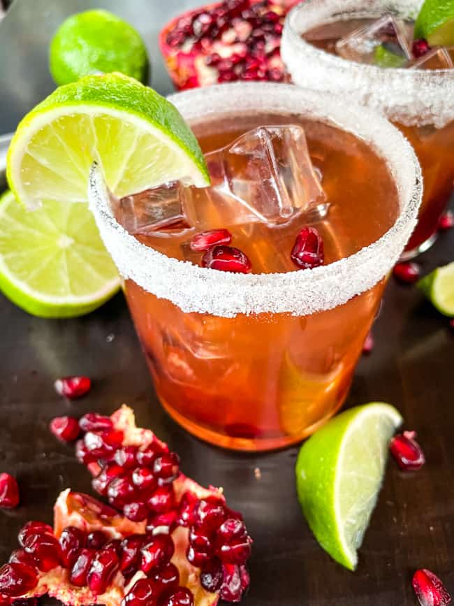 Red tequila cocktail in a sugar rimmed glass with fruit around it