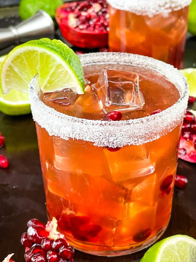 Close up of a Pomegranate Margarita in a short glass with a sugar rim and lime wedge