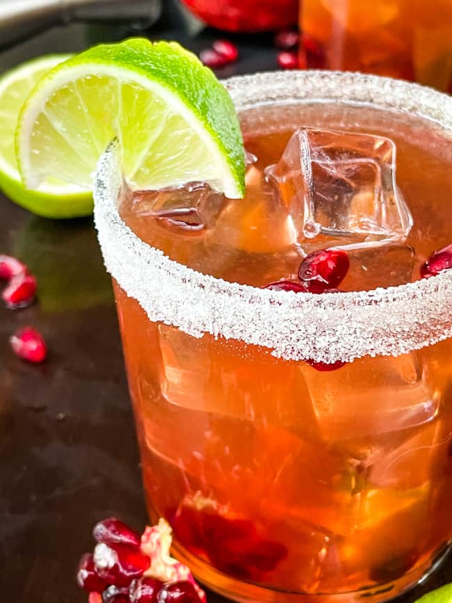 A close up of a Pomegranate Margarita in a short glass with a lime wedge