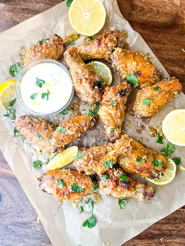 Lemon Pepper Chicken Wings Air Fryer wings scattered on parchment with dipping sauce and lemons