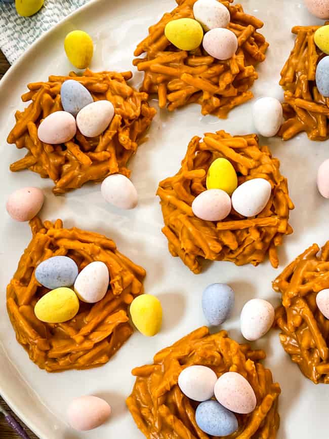 Several Birds Nest Cookies on a white plate with mini eggs in and around the nests