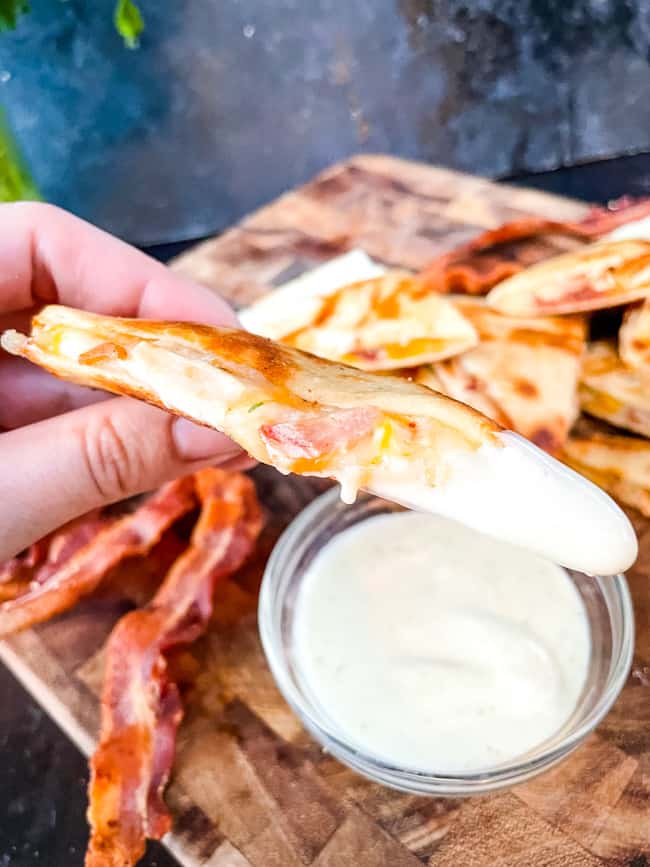 A hand holding a quesadilla with ranch on it