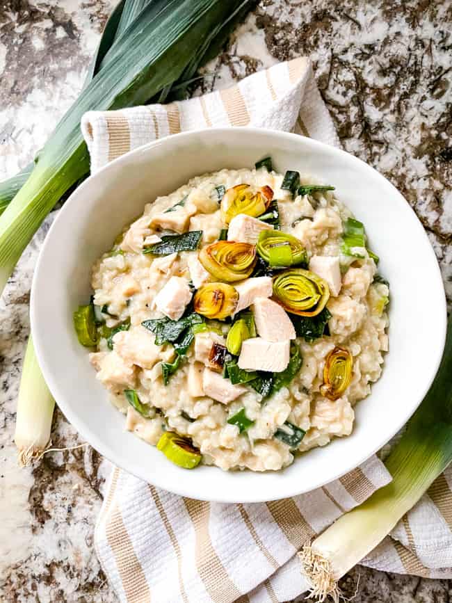 Chicken and Leek Risotto in a white bowl with a tan striped towel under it